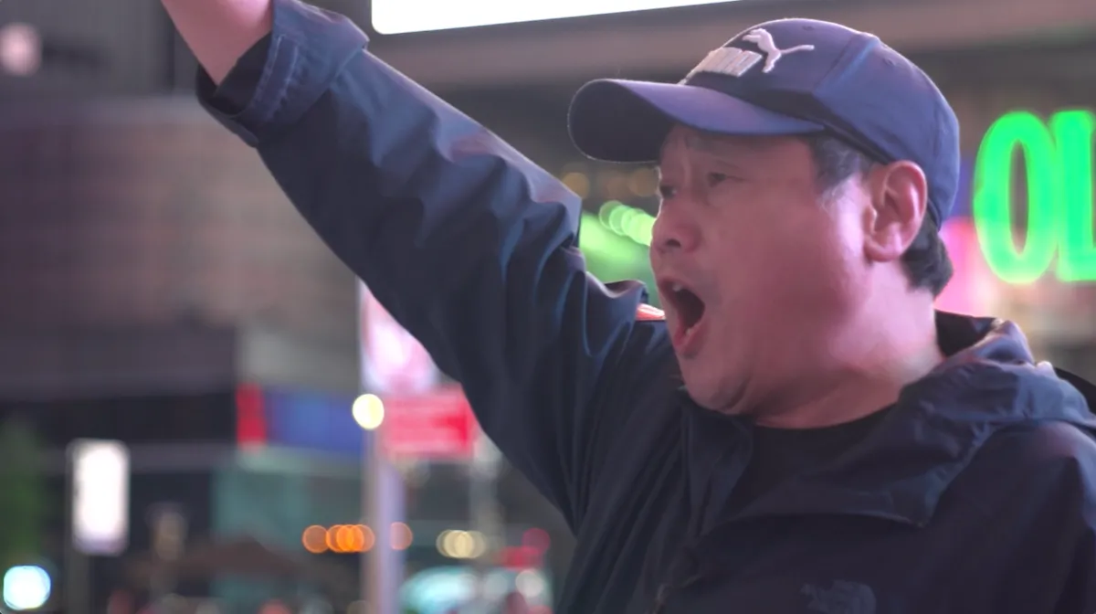 A person in an inner city raises their arms and enthusiastically yells in protest.