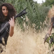 Two women, both with long brown hair and wearing sleeveless vests, perform on their electric guitars in a field of uncut wheat and grass. From Rita Baghdadi's 'Sirens," which is showing in theaters through Oscilloscope Laboratories. Courtesy of Oscilloscope Laboratories . 