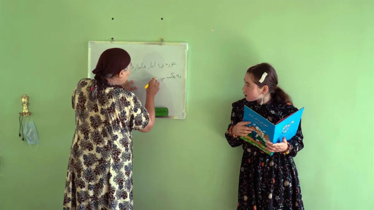 Film still from 'Writing Hawa' featuring two women - one with a book in hand, the other writing on a whiteboard.